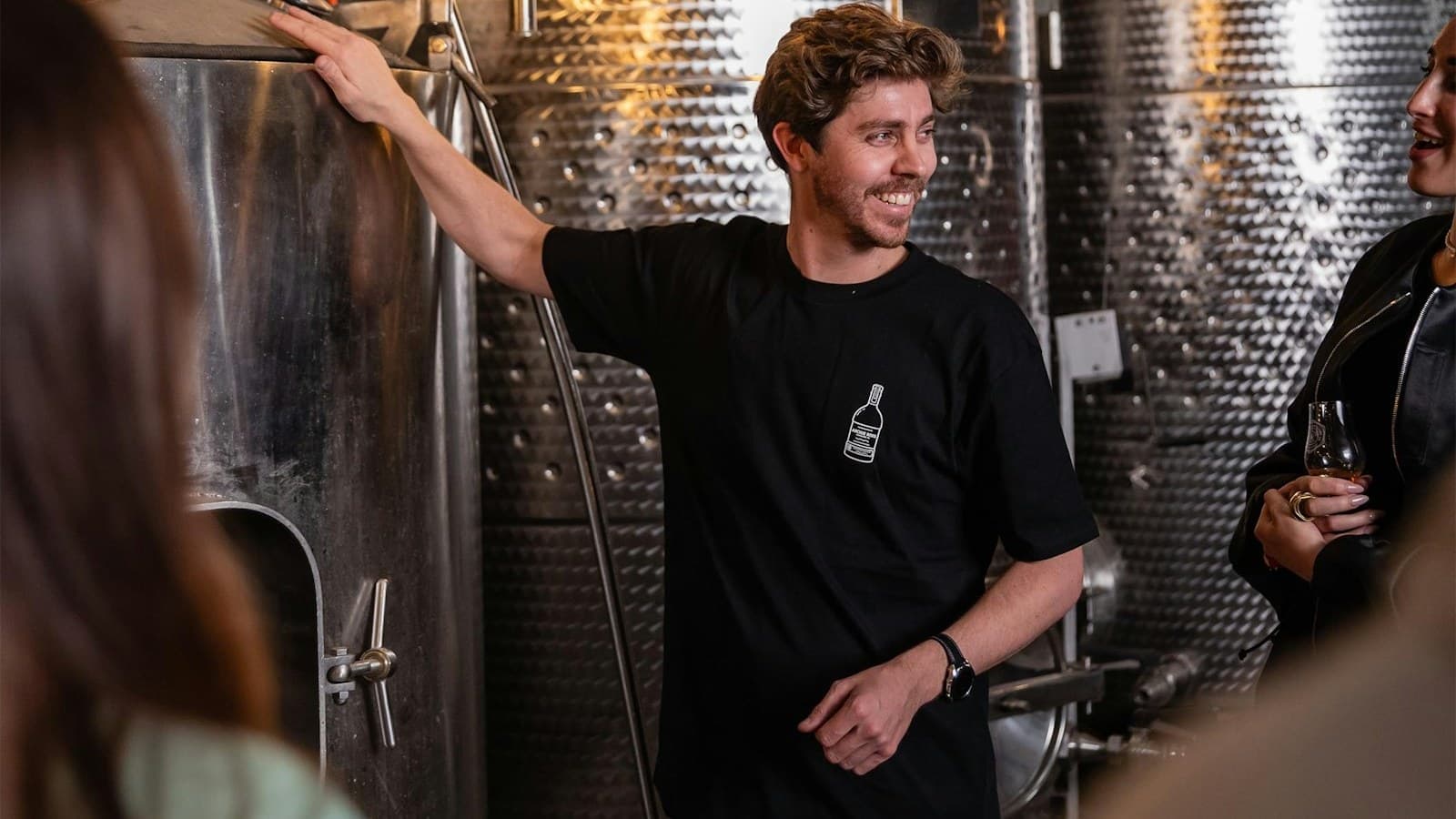 An Archie Rose guide beside the stills, with a guest holding a tasting glass