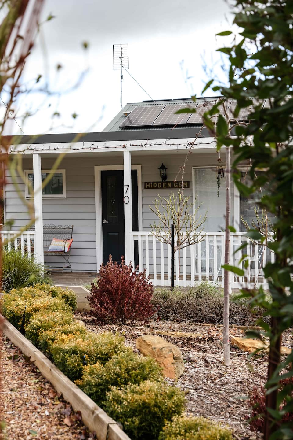 The Hidden Gem cottage in Daylesford, showing its front veranda, dark front door and garden beds